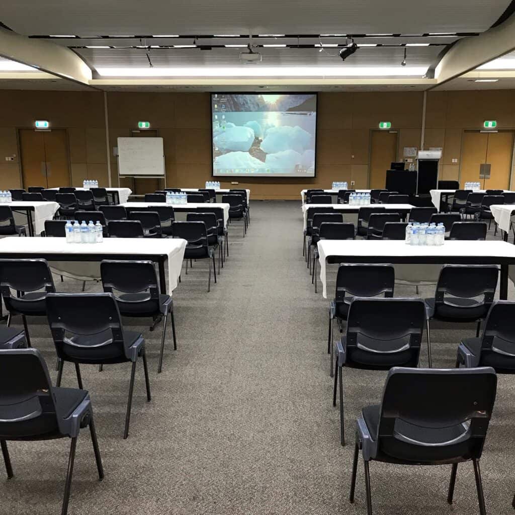 A large room in the conference centre is set up with rows of tables and chairs ready for a training seminar.