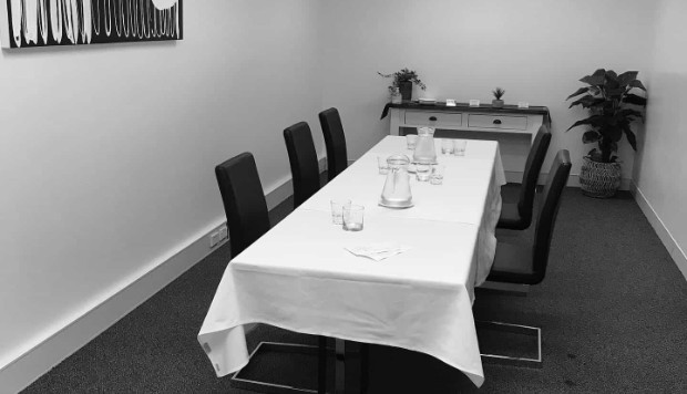 A small private meeting room set up with a table chairs and jugs of water.